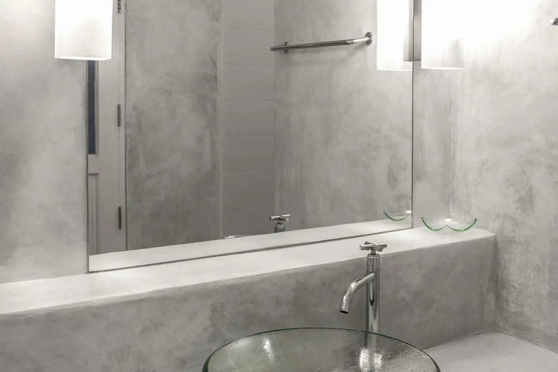 Cuarto de baño con paredes y superficie de la encimera de microcemento de color gris.